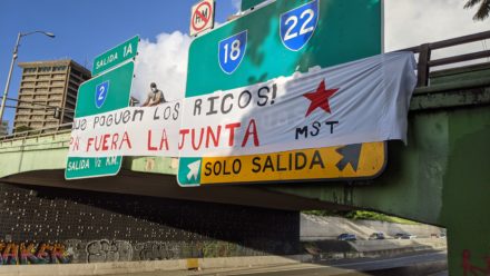 Pancarta desplegada sobre expreso que lee: "¡Que paguen los ricos! Pa' Fuera la Junta"