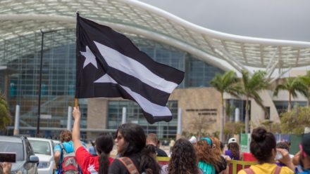 Bandera negra y blanca de Puerto Rico ondeando en una manifestación frente al Centr de Convenciones