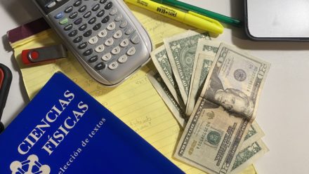 Escritorio de un estudiante con una calculadora, dinero, una libreta y un libro